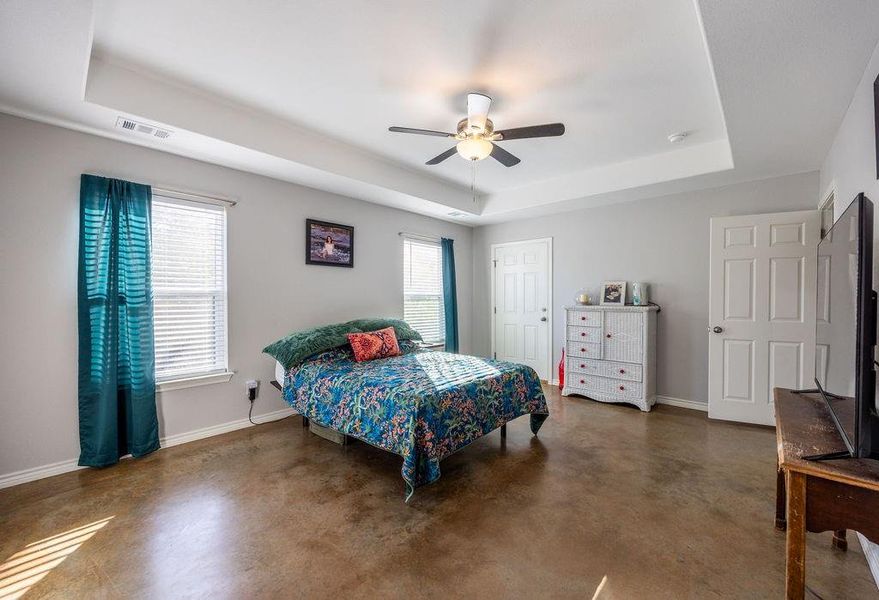 Bedroom with a tray ceiling, multiple windows, finished concrete floors, and ceiling fan