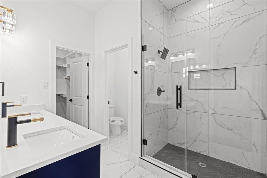 Full bath featuring a marble finish shower, double vanity, and light marble finish floors