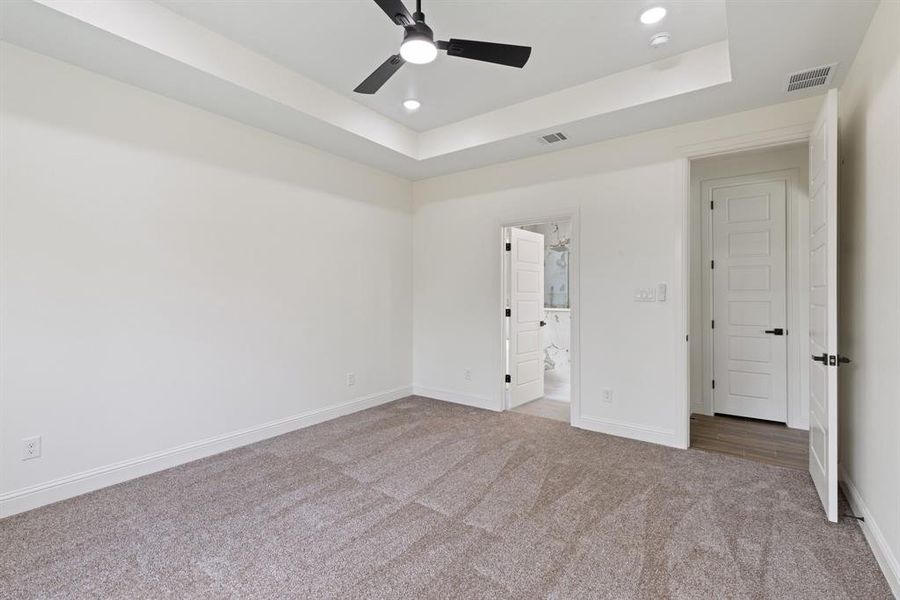 Unfurnished bedroom featuring carpet flooring, a raised ceiling, recessed lighting, ensuite bath, and ceiling fan