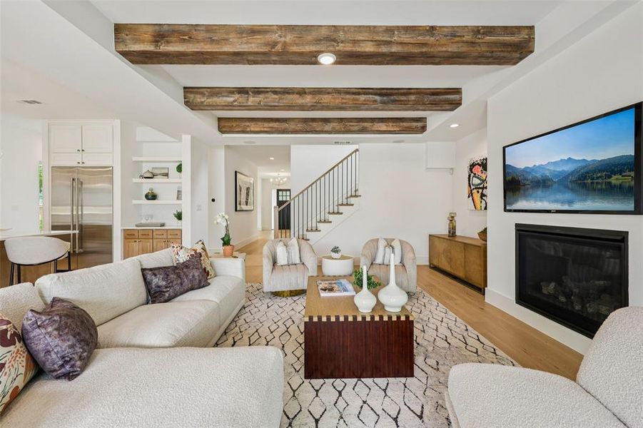 Living area featuring exposed wood-finish ceiling beams, wood-finish flooring, a built-in electric fireplace, and white built-in shelving