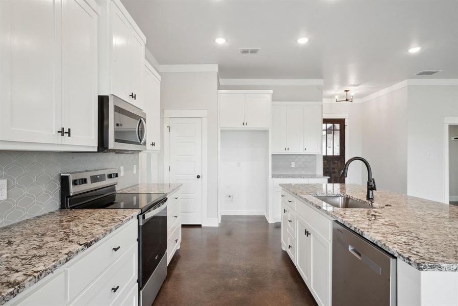 Kitchen with stainless steel appliances, sink, light stone counters, decorative backsplash, and a kitchen island with sink