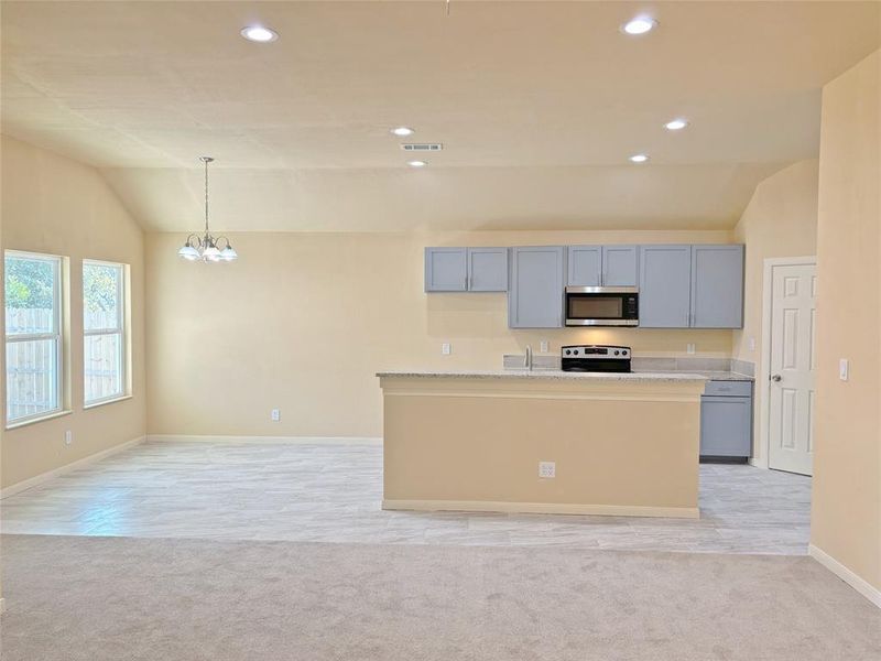 Kitchen featuring vaulted ceiling, an island with sink, light colored carpet, appliances with stainless steel finishes, and a chandelier
