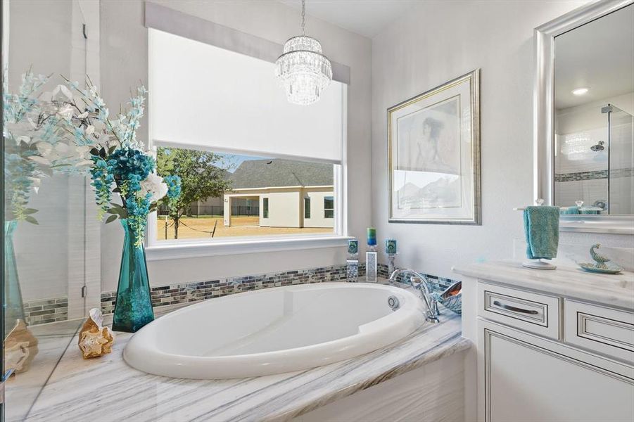 Built-in soaking tub with polished chrome fixtures, surrounded by a natural stone countertop and mosaic tile backsplash