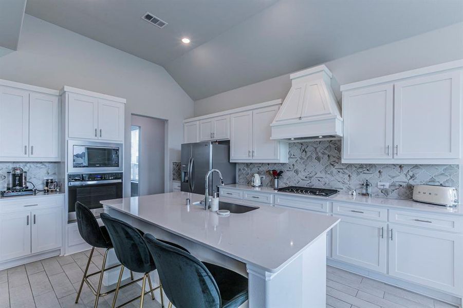 Kitchen featuring a center island with sink, stainless steel appliances, lofted ceiling, white cabinets, and a breakfast bar Kitchen featuring a center island with sink, stainless steel appliances, lofted ceiling, white cabinets, and a breakfast bar