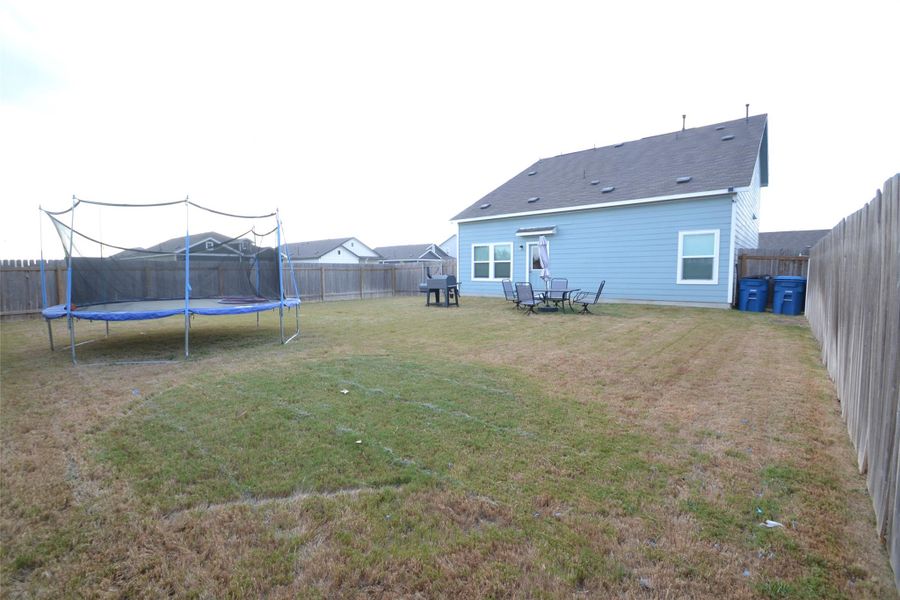 Back of property with a fenced backyard, a patio area, and a trampoline