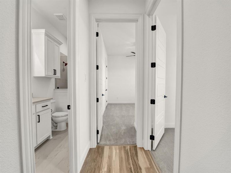 Hallway with light wood finished floors, visible vents, and baseboards Hallway with light wood finished floors, visible vents, and baseboards