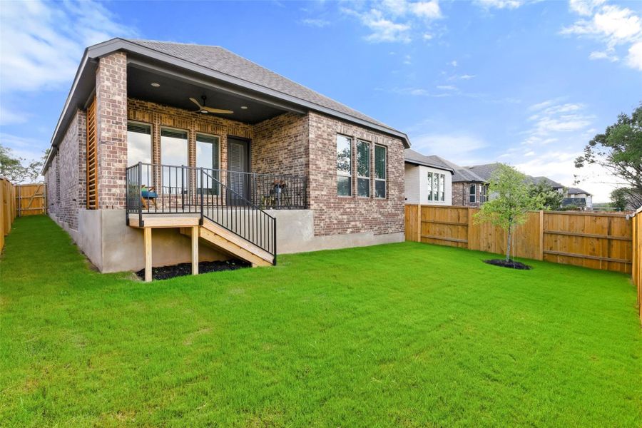 Expansive backyard featuring a covered patio with a ceiling fan, a private wooden fence, a small tree, and a brick exterior