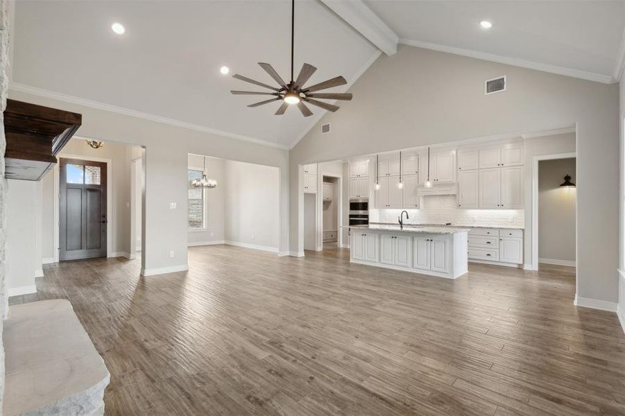 Unfurnished living room with crown molding, ceiling fan with notable chandelier, light wood-type flooring, and high vaulted ceiling