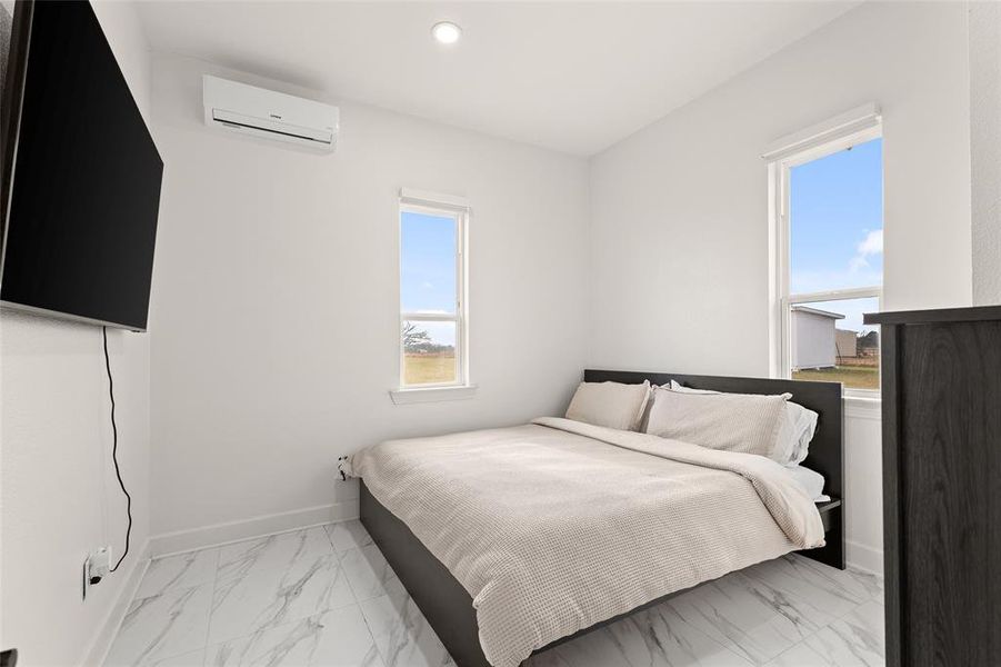 Bedroom featuring a wall-mounted mini-split system, recessed ceiling lighting, and two windows Bedroom featuring a wall-mounted mini-split system, recessed ceiling lighting, and two windows