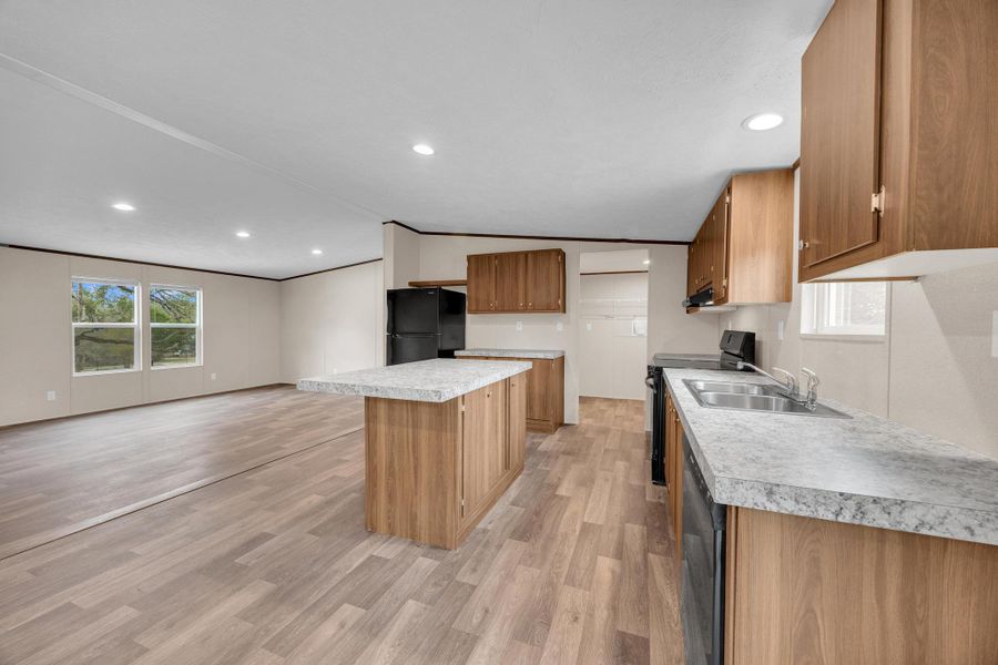 Kitchen with black appliances, light countertops, light wood finished floors, open floor plan, and a kitchen island