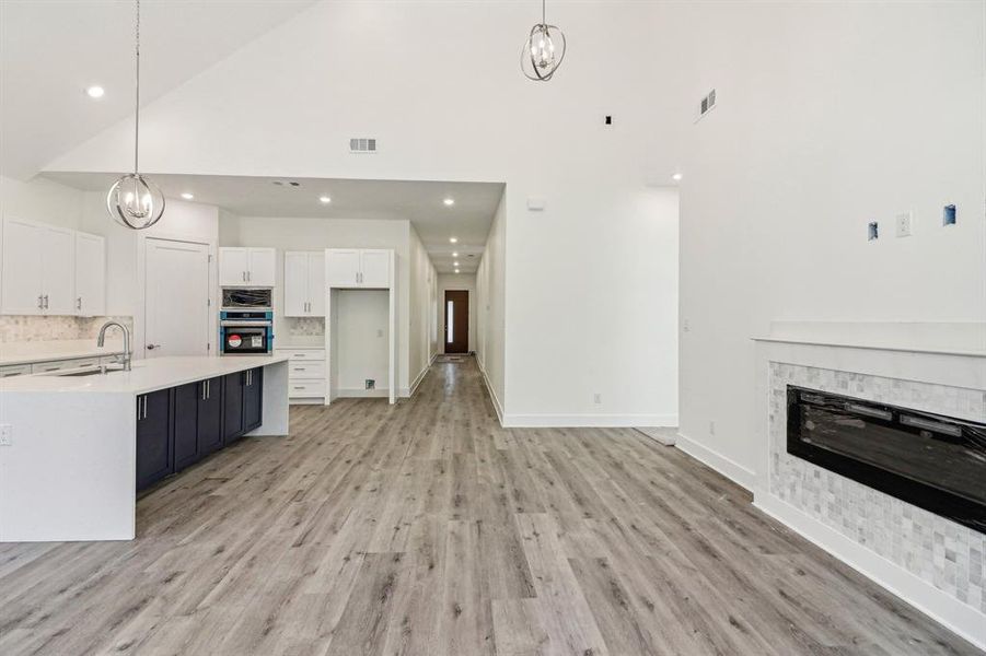 Kitchen featuring a chandelier, high vaulted ceiling, white cabinetry, hanging light fixtures, and backsplash Kitchen featuring a chandelier, high vaulted ceiling, white cabinetry, hanging light fixtures, and backsplash