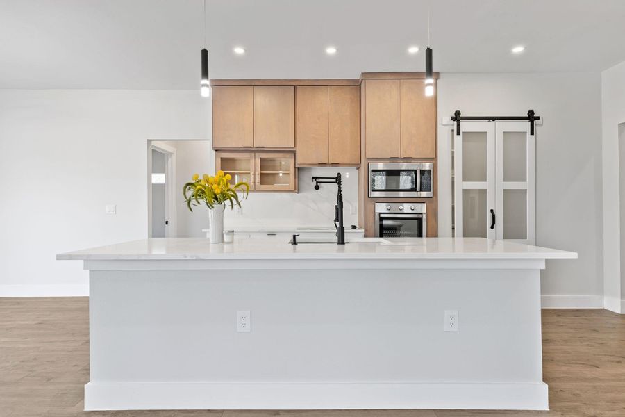 Kitchen with light wood-style flooring, light brown cabinetry, a barn door, light stone counters, and a large island with sink