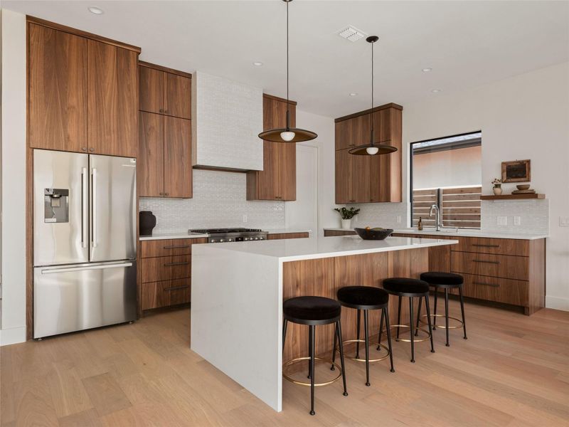 Kitchen with modern cabinets, appliances with stainless steel finishes, decorative backsplash, a breakfast bar area, and hanging light fixtures