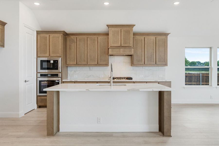 Kitchen with tan wood cabinets, marble backsplash, quartz island, and stainless steel double oven Kitchen with tan wood cabinets, marble backsplash, quartz island, and stainless steel double oven