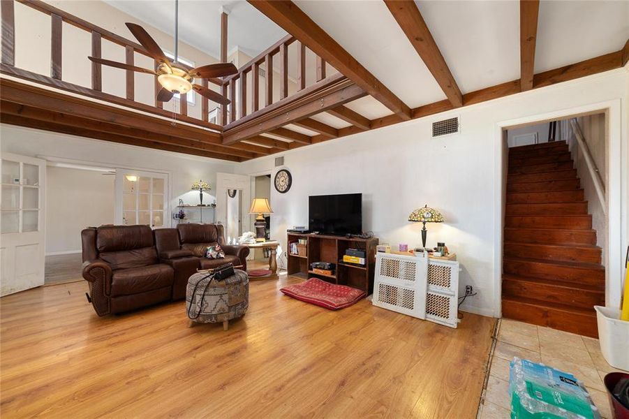 Living room with ceiling fan, a towering ceiling, light hardwood / wood-style flooring, and beamed ceiling