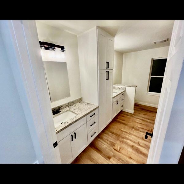Functional bathroom featuring a double vanity with ample storage and sleek wood flooring.