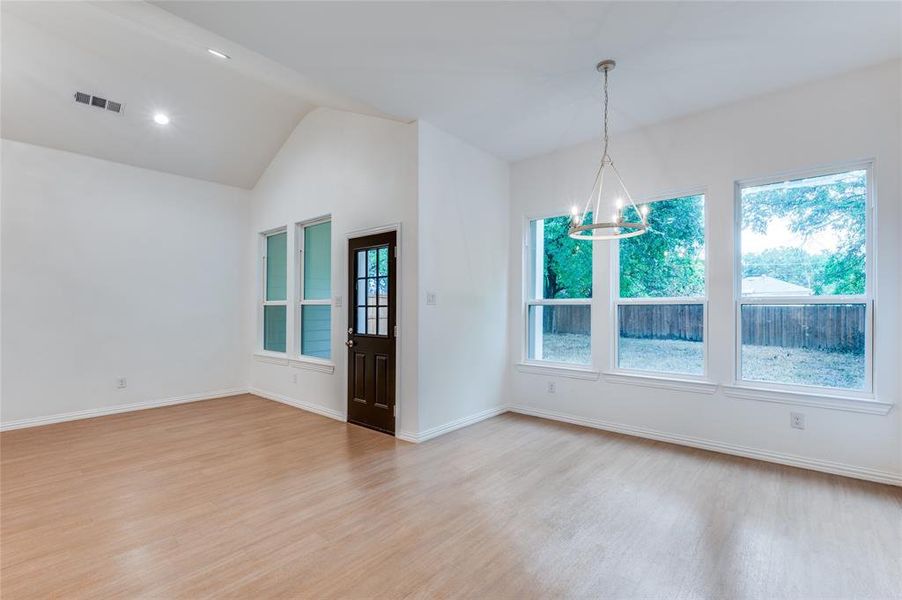 Spare room featuring light wood-type flooring, lofted ceiling, and a healthy amount of sunlight