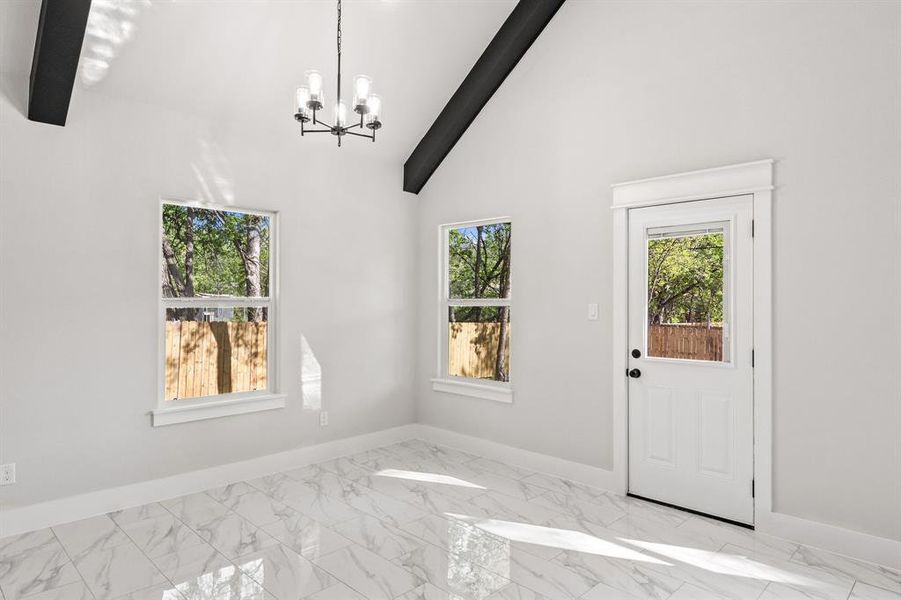 Dual tone kitchen with light stone countertops, an island with sink, light marble finish flooring, vaulted ceiling with beams, and two tone cabinetry