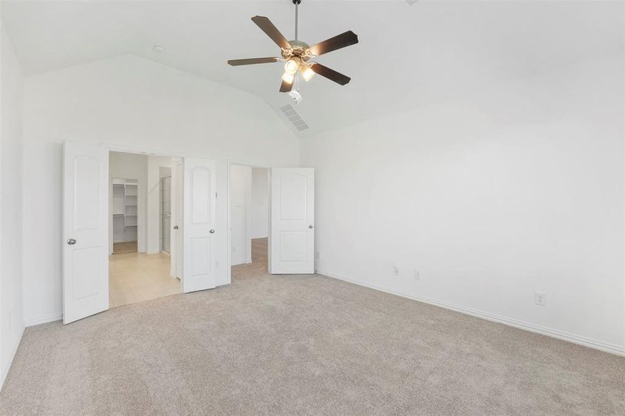 Unfurnished bedroom featuring ceiling fan, high vaulted ceiling, a walk in closet, a closet, and light carpet