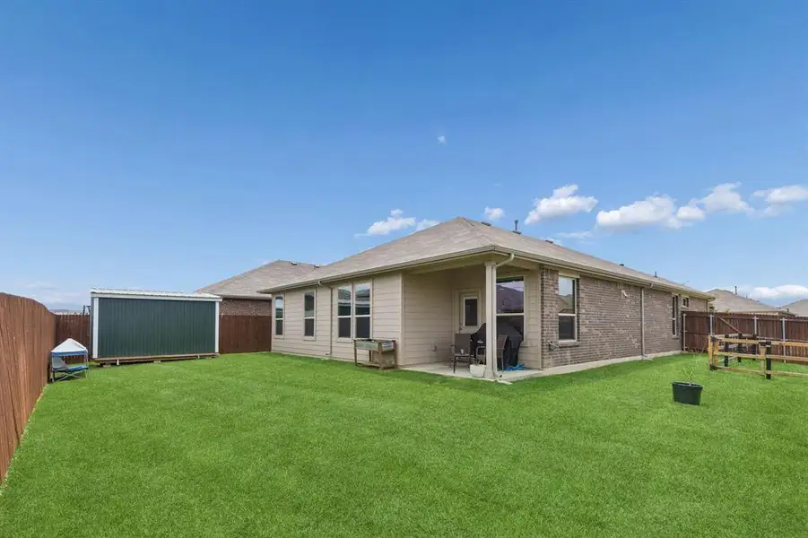 Expansive fenced backyard featuring a covered patio, a green storage shed, and a large grassy area