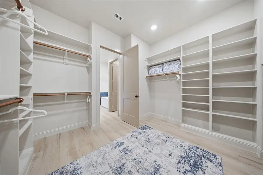 Spacious walk-in closet featuring extensive built-in shelving, dual hanging rods, wood-finish flooring, and recessed lighting