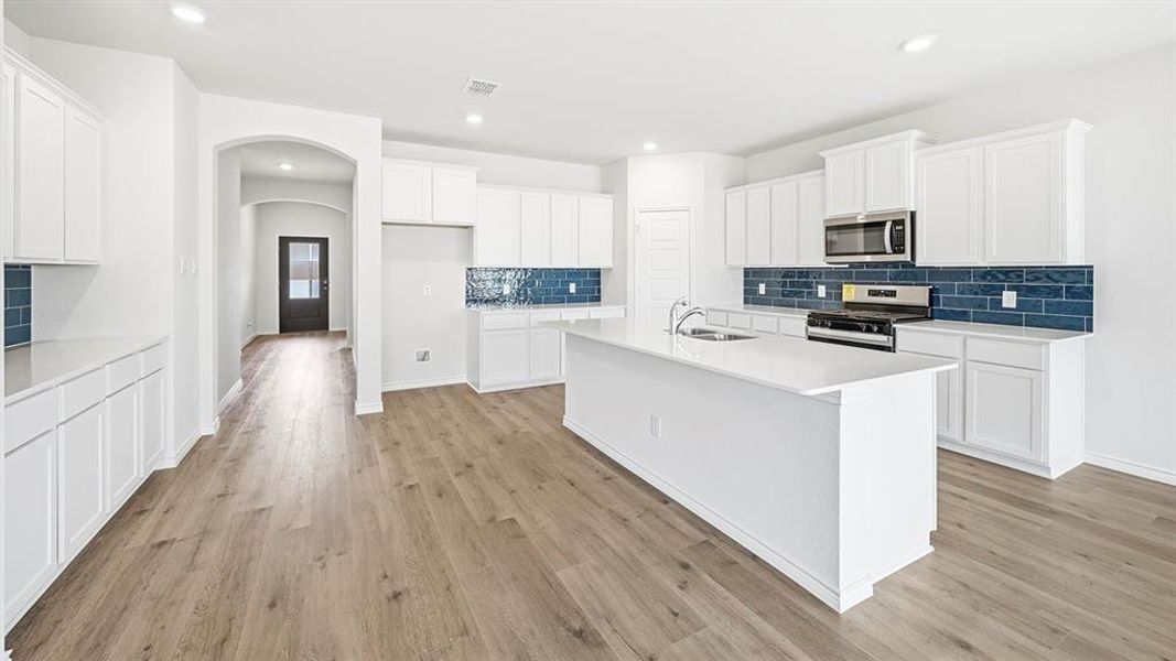 Kitchen featuring white cabinets, stainless steel appliances, arched walkways, an island with sink, and backsplash