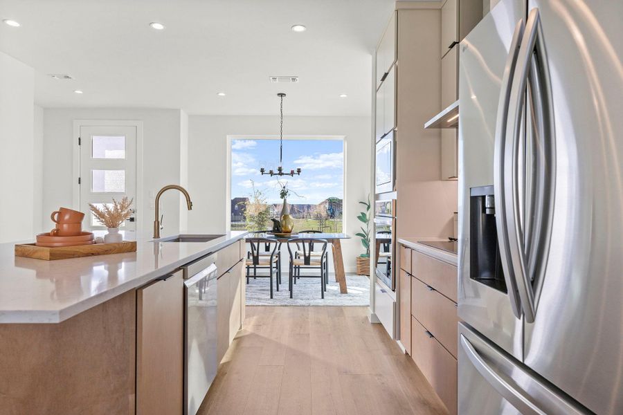 Kitchen with stainless steel appliances, light wood-style floors, modern cabinets, light stone counters, and pendant lighting