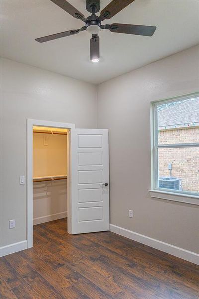 Unfurnished bedroom with a spacious closet, dark wood-type flooring, and a ceiling fan Unfurnished bedroom with a spacious closet, dark wood-type flooring, and a ceiling fan