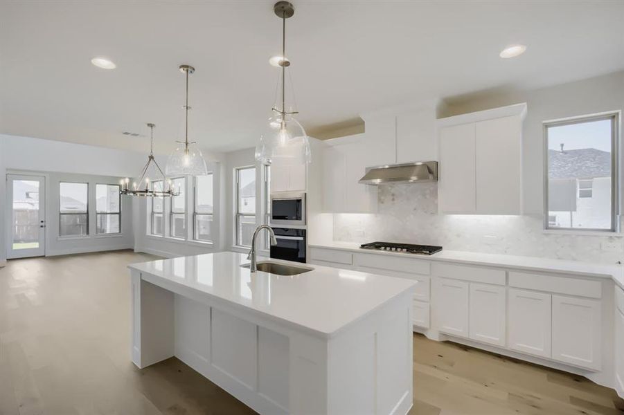 Modern kitchen featuring a large island with sink, white cabinetry, integrated stainless steel appliances, and a gas cooktop