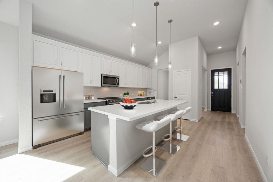 A chef's kitchen featuring a large central island with seating, sleek white shaker-style cabinetry, and durable, wood-look flooring. This bright and modern space, perfect for entertaining, includes stainless steel appliances, a built-in microwave, and elegant pendant lighting over the island. The open floor plan seamlessly flows into adjacent living areas, enhanced by ample natural light and neutral gray wall tones. A chef's kitchen featuring a large central island with seating, sleek white shaker-style cabinetry, and durable, wood-look flooring. This bright and modern space, perfect for entertaining, includes stainless steel appliances, a built-in microwave, and elegant pendant lighting over the island. The open floor plan seamlessly flows into adjacent living areas, enhanced by ample natural light and neutral gray wall tones.