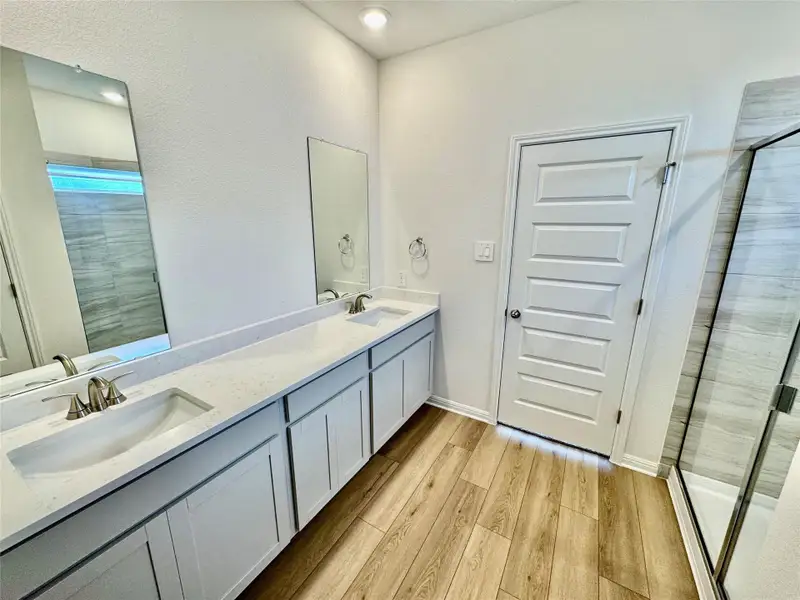 Full bathroom with double vanity, light wood-style flooring, and a shower stall Full bathroom with double vanity, light wood-style flooring, and a shower stall