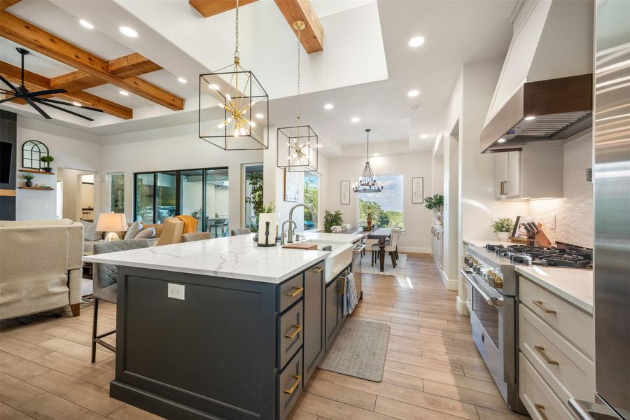 Kitchen with decorative light fixtures, white cabinets, custom exhaust hood, a large island with sink, and stainless steel appliances Kitchen with decorative light fixtures, white cabinets, custom exhaust hood, a large island with sink, and stainless steel appliances