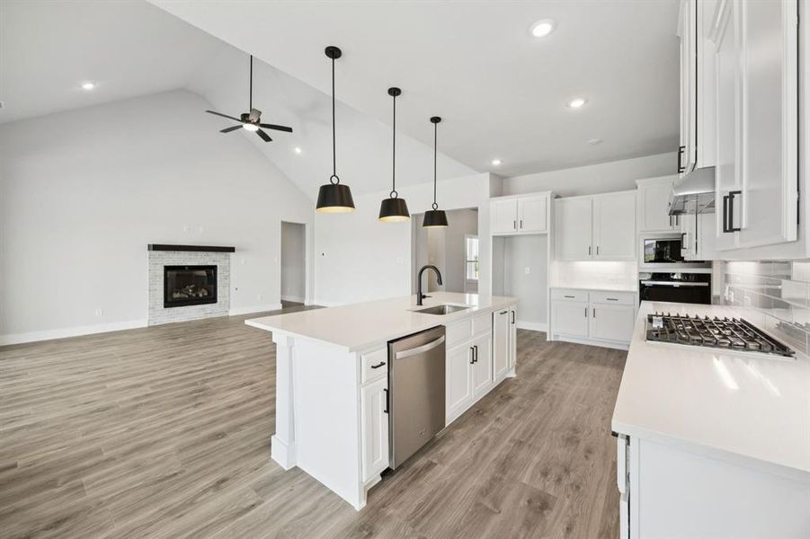 Kitchen featuring white cabinets, high vaulted ceiling, appliances with stainless steel finishes, a glass covered fireplace, and light wood-style floors