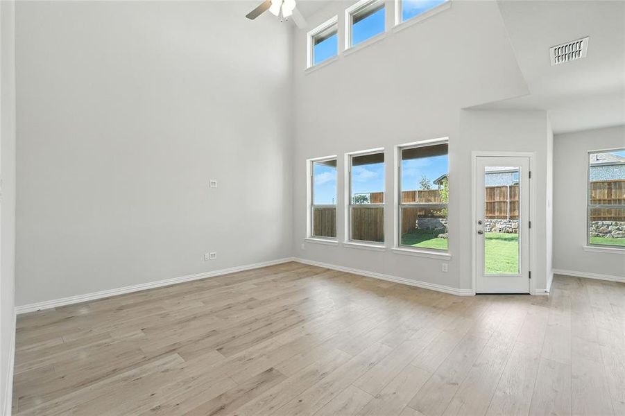 Unfurnished room featuring ceiling fan, light wood-type flooring, and a towering ceiling Unfurnished room featuring ceiling fan, light wood-type flooring, and a towering ceiling