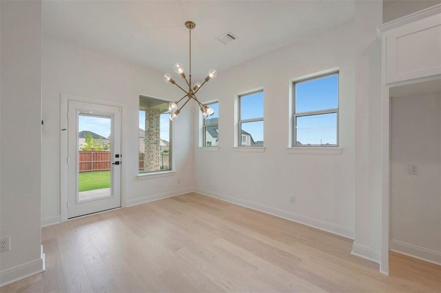 Bright interior space featuring light wood-finish flooring, multiple windows, a rear glass-paneled door, and a modern brass chandelier