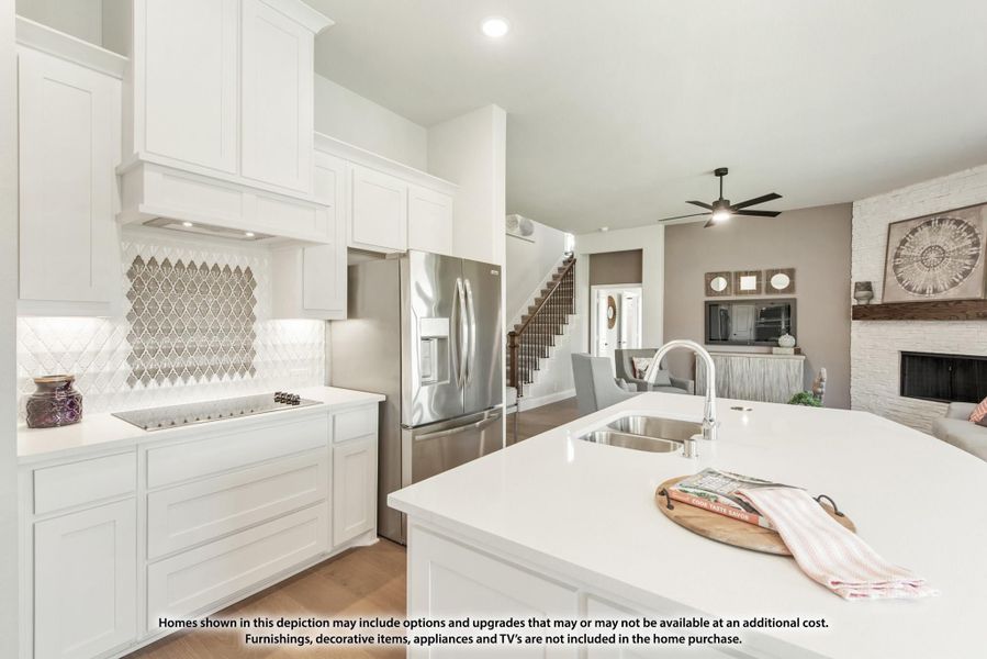 White kitchen with island, stainless steel appliances, decorative tile backsplash, and open view to living room with fireplace.