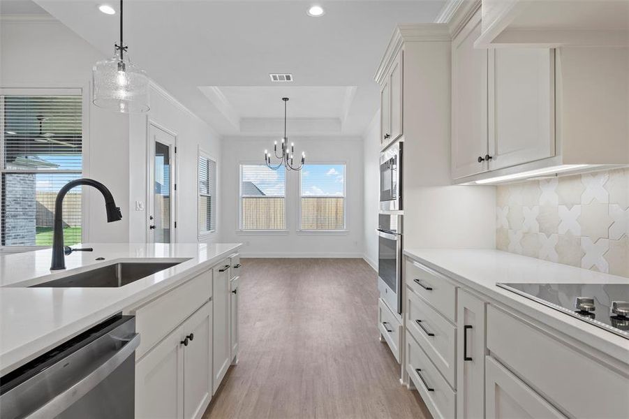 Kitchen with white cabinetry, decorative light fixtures, appliances with stainless steel finishes, a raised ceiling, and recessed lighting Kitchen with white cabinetry, decorative light fixtures, appliances with stainless steel finishes, a raised ceiling, and recessed lighting