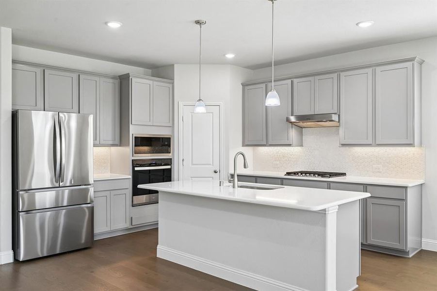 Kitchen featuring a central island with a sink, grey shaker-style cabinetry, stainless steel appliances, white countertops, and wood-finish flooring Kitchen featuring a central island with a sink, grey shaker-style cabinetry, stainless steel appliances, white countertops, and wood-finish flooring