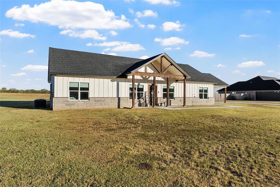 Back of house with board and batten siding, a yard, and roof with shingles