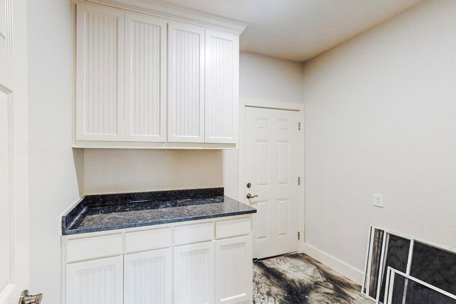 with dark stone countertops, white cabinetry, and light wood-type flooring