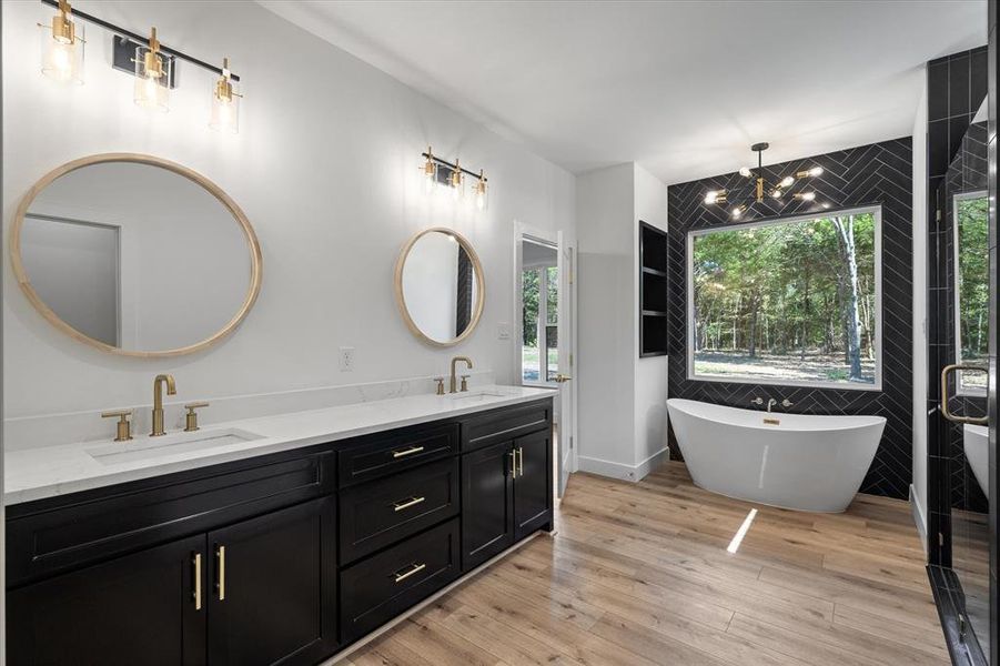 Full bath with a freestanding bath, double vanity, light wood finished floors, tile walls, and a chandelier