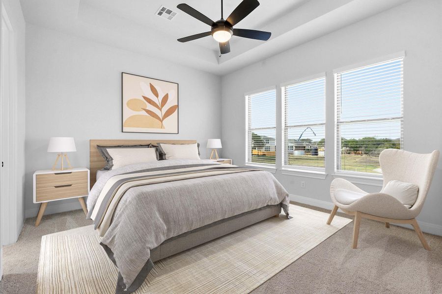 Bedroom with a raised ceiling, light colored carpet, and a ceiling fan