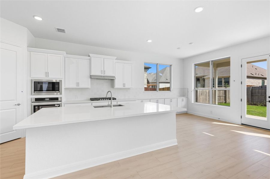 Kitchen featuring white cabinets, recessed lighting, decorative backsplash, stainless steel oven, and an island with sink