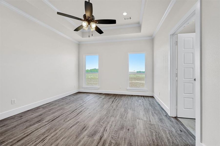 Empty room featuring ceiling fan, a raised ceiling, hardwood / wood-style flooring, and crown molding