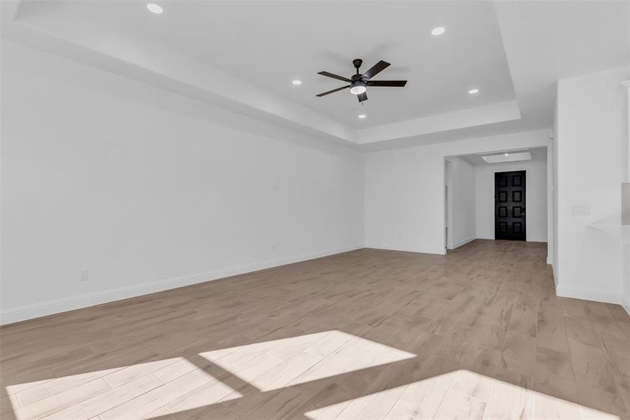 Living room with a tray ceiling, recessed lighting, light wood finished floors, and a ceiling fan