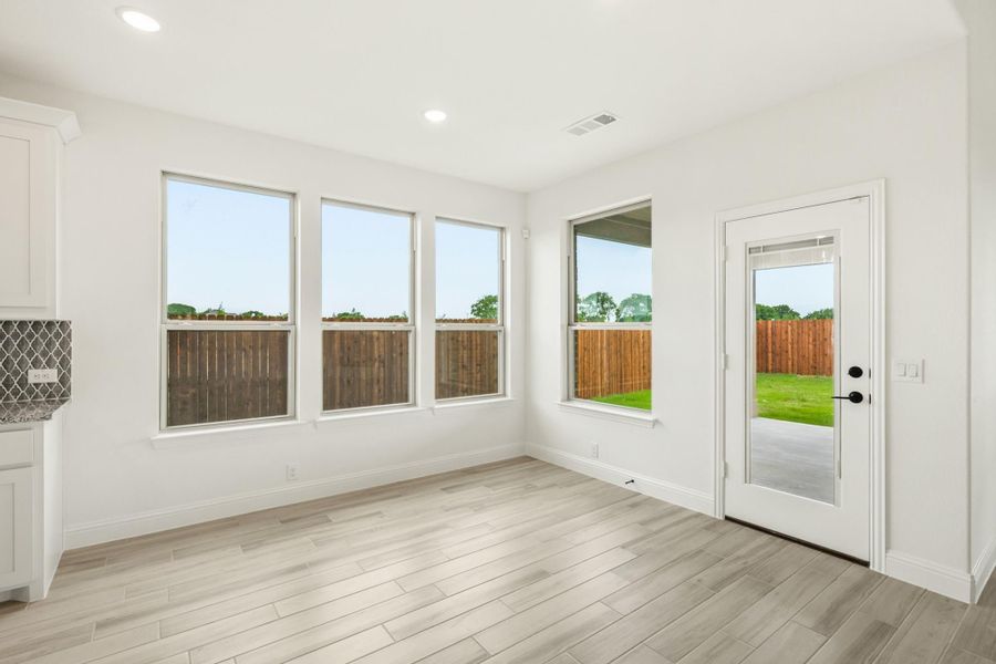 Bright dining area with light wood floors, four large windows, and glass back door overlooking fenced yard Bright dining area with light wood floors, four large windows, and glass back door overlooking fenced yard