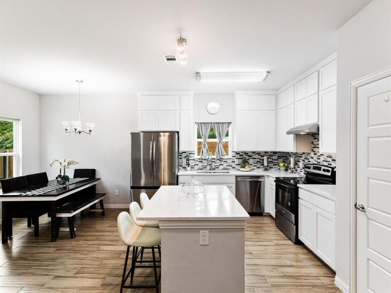 Bright kitchen featuring white cabinetry, stainless steel appliances, a tile backsplash, and a central island with countertop seating
