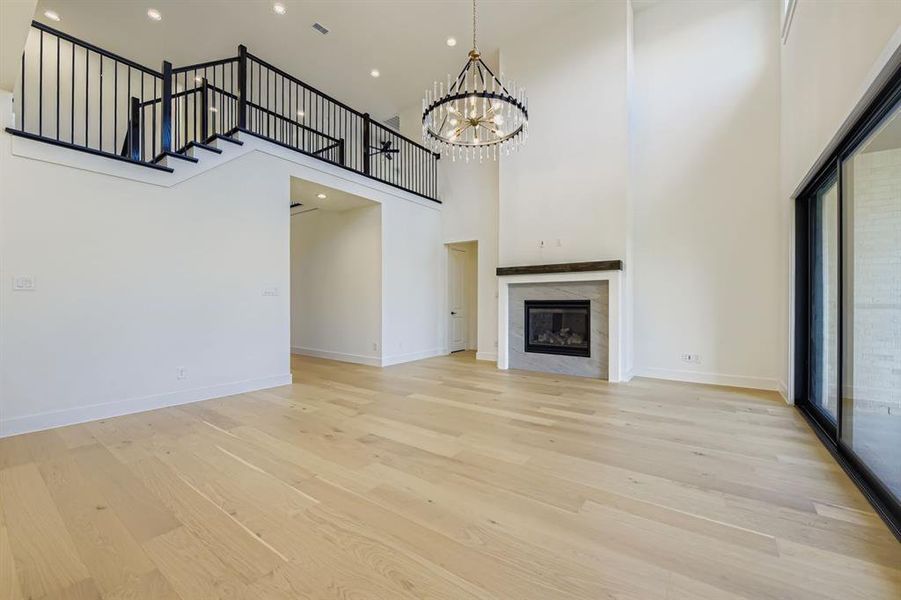 Unfurnished living room with a high ceiling, a tiled fireplace, light wood-type flooring, a chandelier, and recessed lighting Unfurnished living room with a high ceiling, a tiled fireplace, light wood-type flooring, a chandelier, and recessed lighting