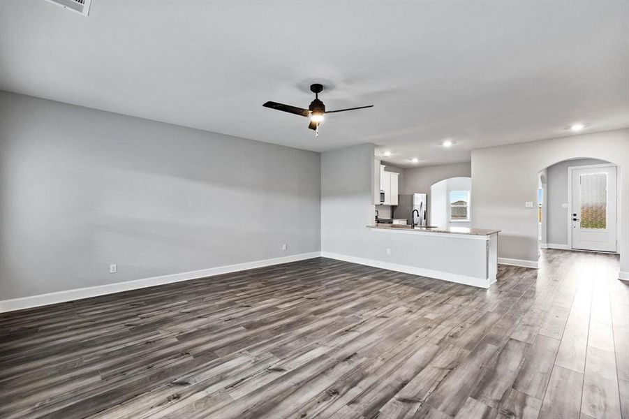 Unfurnished living room featuring arched walkways, ceiling fan, recessed lighting, dark wood-style flooring, and baseboards