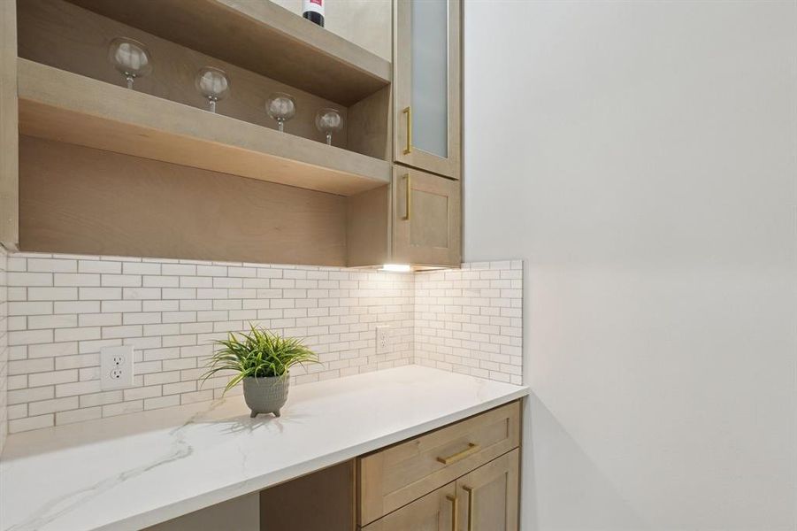 Kitchen with open shelves, backsplash, light stone countertops, glass fronted cabinets, and light wood finish cabinets